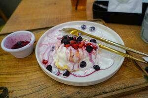 Reste hausgemacht flauschige japanisch Pfannkuchen mit Beere Soße und Eis Sahne Belag auf ein Weiß Teller foto