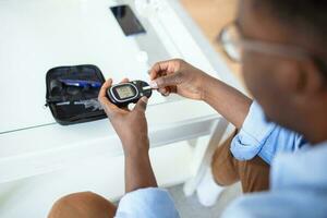 jung afrikanisch Mann mit Digital Glukometer beim heim. Diabetes Steuerung foto