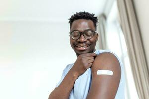 covid-19 Impfung. Porträt von glücklich geimpft afrikanisch Mann zeigen seine Arm nach Coronavirus antiviral Impfstoff Schuss . covid Immunisierung Kampagne Konzept. foto