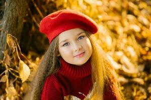 schön Mädchen im ein rot Baskenmütze ist Sitzung in der Nähe von ein Baum im Herbst foto