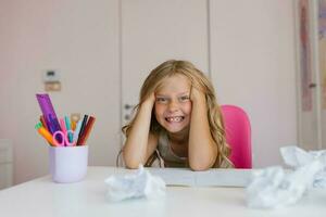 komisch kaukasisch Mädchen von Sieben Jahre alt beim ihr Schreibtisch beim Zuhause oder beim Schule müde von tun Hausaufgaben foto