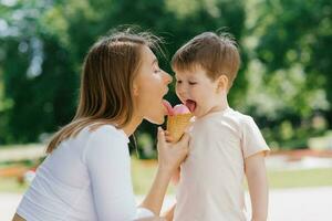 jung kaukasisch Mutter mit ein wenig Junge Essen Eis Sahne draußen. Sommer- Essen und kostenlos Zeit foto