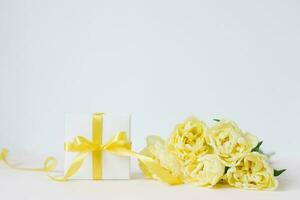Frühling Komposition von ein Strauß von Gelb Tulpen, ein Geschenk mit ein Gelb Bogen und Band auf ein Weiß Hintergrund. Frühling, Damen Tag, Mamas Tag, Geburtstag. Vorderseite Sicht, Kopieren Raum foto