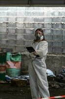 Notfall Verschmutzung Fabrik Konzept. weiblich Chemiker tragen ppe und Gas Maske inspizieren Öl auf Fabrik Fußboden foto