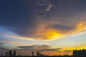 Silhouette von Bangkok bei Sonnenuntergang mit dem Flugzeug, das im Dämmerungshimmel fliegt foto