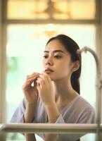 attraktiv Frische asiatisch Frau sauber Gesicht frisch Wasser mit Pflege aussehen zu Spiegel im Badezimmer Zuhause Konzept durch ai generiert foto