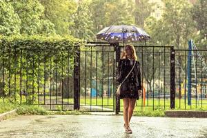 eine junge frau steht im regen auf der straße unter einem regenschirm. regnerischen Tag foto