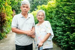 glücklich Senior Paar Gehen zusammen im das Garten. alt Alten mit ein Gehen Stock zu Hilfe gehen Gleichgewicht. Konzept von Liebe und Pflege von das Familie und Gesundheit Versicherung zum Familie foto