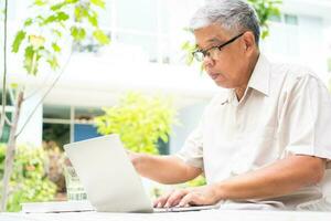 Porträt von alt Alten asiatisch Mann mit ein Computer Laptop im das Hinterhof zum Lernen Neu Fertigkeit nach im Ruhestand. Konzept von Nein Altersdiskriminierung und nicht Sein spät zum Lernen. foto