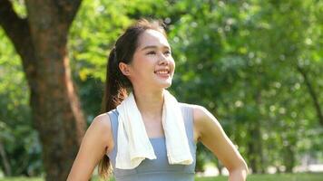 Porträt jung asiatisch Frau attraktiv lächelnd und verwenden Weiß Handtuch ruhen nach trainieren. lächelnd sportlich jung Frau Arbeiten aus draußen und suchen beim Kamera. gesund Lebensstil Gut Sein Wellness foto