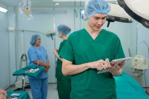 Porträt von asiatisch der Chirurg mit medizinisch Maske Stehen und halten ein Tablette im Betrieb Theater beim ein Krankenhaus. Mannschaft von Fachmann Chirurgen. Gesundheitspflege, Notfall medizinisch Bedienung Konzept foto