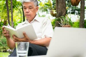Senior alt Mann lesen ein Buch im das Park und Trinken Wasser. Konzept von Pensionierung Lebensstil und Hobby. foto