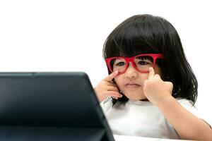 Kleines asiatisches Vorschulmädchen mit roter Brille und Tablet-PC auf weißem Hintergrund, asiatisches Mädchen, das mit einem Videoanruf mit einem Tablet spricht und lernt, Bildungskonzept für Schulkinder. foto