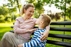 glücklich Mutter ist Sitzung mit ihr Sohn auf Bank im Park. Sie sind haben Spaß zusammen. foto