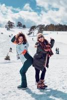 Zwei glückliche Frauen, die am sonnigen Wintertag im Schnee stehen und Spaß haben.