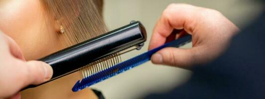 ein Friseur ist begradigen das Haar von das jung Brünette Frau im ein Schönheit Salon. foto