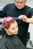 ein Friseur ist Trocknen das Rosa Haar von das jung Frau im ein Schönheit Salon. foto