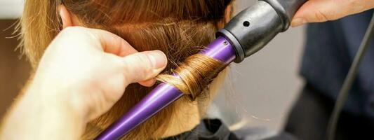 schließen oben von Haar-Stylisten Hände mit ein Eisstockschießen Eisen zum Haar Locken im ein Schönheit Salon. foto