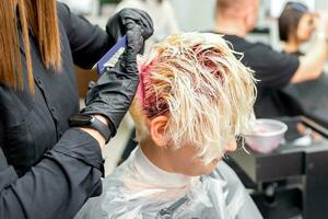 das Fachmann Friseur Verwendet ein Bürste zu anwenden das Rosa Farbstoff zu das Haar. Haar Färbung Konzept. foto