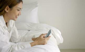 entspannt Frau mit Clever Telefon im das Morgen im Bett beim heim. foto