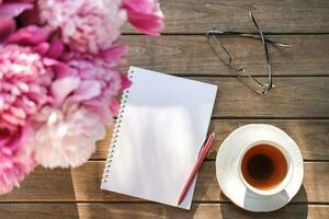 Notizblock, Stift und Tee Tasse auf ein hölzern Tisch. machen ein machen aufführen oder Einkaufen Liste. Wunschzettel, Wiedergabeliste foto