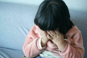 ein verärgert Kind Mädchen Startseite ihr Gesicht mit Hand Sitzung auf Sofa beim Zuhause foto