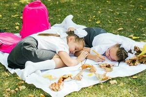 zwei süß Schulmädchen wurden müde von tun ihr Hausaufgaben und fiel schlafend auf ein Decke im ein sonnig Herbst Park. draussen Bildung. zurück zu Schule Konzept foto