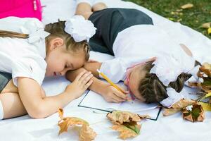 zwei süß Schulmädchen habe müde von tun ihr Hausaufgaben und fiel schlafend auf ein Decke. draussen Bildung. zurück zu Schule Konzept foto