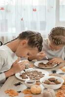 vorbereiten zu feiern Halloween und vorbereiten ein behandeln. zwei Mädchen schmücken Halloween Lebkuchen Kekse auf Platten mit Schokolade Glasur. Lebensstil foto