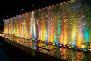 Wasser fallen auf das Stein Wand, Brunnen mit schön mehrfarbig Orange Erleuchtung beim Nacht. foto