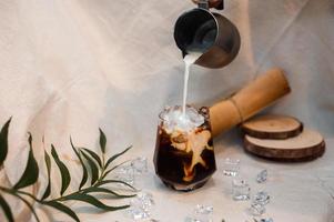 Barista gießt Milch in ein Glas Eiskaffee