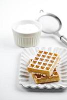 belgische Waffeln mit Zuckerpulver auf Keramikplatte und Sieb auf weißem Tisch. foto