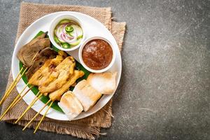 Schweinefleisch-Satay mit Erdnusssauce und Gurken, Gurkenscheiben und Zwiebeln in Essig foto