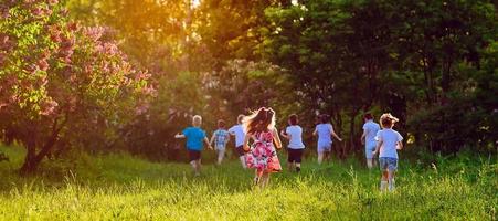 Eine Gruppe glücklicher Kinder von Jungen und Mädchen läuft an einem sonnigen Sommertag im Park auf dem Rasen.
