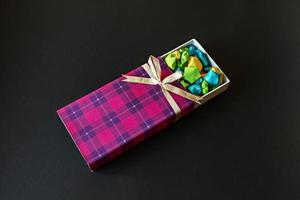 Farbige Geschenkbox mit Satinschleife mit Origami-Papiersternen auf schwarzem Hintergrund. Geschenke für die Feiertage. foto