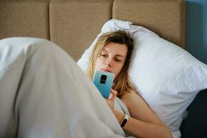 Frau mit Smartphone im das Bett, Sozial Medien, faul Wochenende foto