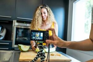 Frau Aufzeichnung mit ein Kamera mögen ein Melone Cutter im ein Küche foto