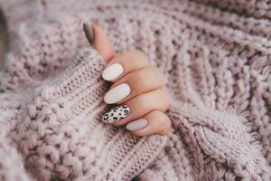 ein Frau Hand mit ein schön Maniküre hält ein Beige Stoff. Herbst Trend, Beige Farbe Polieren mit Leopard Muster auf Nägel mit Gel Polieren, Schellack. foto