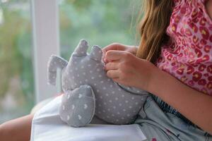 Nahansicht von ein Kinder Hände Nähen ein Sanft Spielzeug in der Nähe von das Fenster. das Mädchen näht oben ein Sanft Spielzeug von ein Elefant. handgefertigt, Hobby. foto