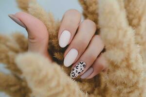 Frau Hand mit ein schön oval geformt Maniküre. Herbst Trend, Beige Farbe Polieren mit Leopard Muster auf Nägel mit Gel Polieren, Schellack. foto