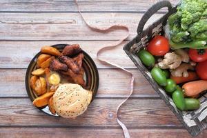 Junk Food, frisches Gemüse und Maßband auf Holztisch foto