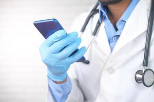 Arzthand in Schutzhandschuhen mit einem Smartphone foto