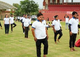 Neu Delhi, Indien, Juni 21, 2023 - - Gruppe Yoga Übung Session zum Menschen beim Yamuna Sport Komplex im Delhi auf International Yoga Tag, groß Gruppe von Erwachsene Teilnahme Yoga Klasse im Kricket Stadion foto