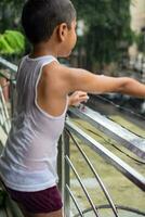 wenig Kind spielen im Sommer- Regen im Haus Balkon, indisch Clever Junge spielen mit Regen Tropfen während Monsun regnerisch Jahreszeit, Kind spielen im Regen foto