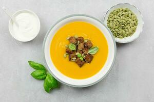 saisonal Herbst geröstet Kürbis und Karotte Suppe mit Sahne und Roggen Brot Croutons auf ein Licht Beton Hintergrund. oben Sicht. foto