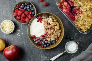 Schüssel von hausgemacht Granola mit Joghurt und frisch Beeren auf dunkel Stein Beton Hintergrund. Cranberry und Apfel zerbröckeln, knackig mit Mandel Flocken und Hafer. oben Sicht. foto