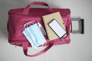 Smartphone, Reisepass, Händedesinfektionsmittel und Gesichtsmaske auf Koffer am Boden foto