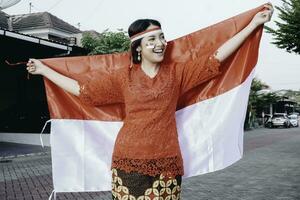 glücklich lächelnd indonesisch Frau tragen rot Kebaya halten Indonesiens Flagge zu feiern Indonesien Unabhängigkeit Tag. draussen Fotoshooting Konzept foto
