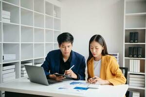 asiatischer geschäftskollege präsentiert und erklärt und verwendet laptop und tablet. Teamarbeit, Finanzmarketing-Team, während Sie in einem modernen Büroraum sitzen. foto