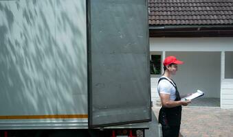 Lieferung Mann im Uniform und Deckel mit Zwischenablage Stehen in der Nähe von das LKW foto